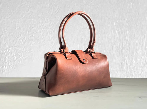 Warm Faded Tan Structured Vintage Frame Satchel With Dual Curved Top Hand Grips, Central Snap Tab Closure And Rear Horizontal Zipper Slip Pocket
